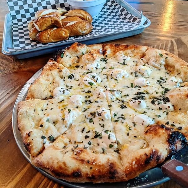 White pizza with dollops of ricotta and herbs, alongside a tray of pretzel bites and dip.
