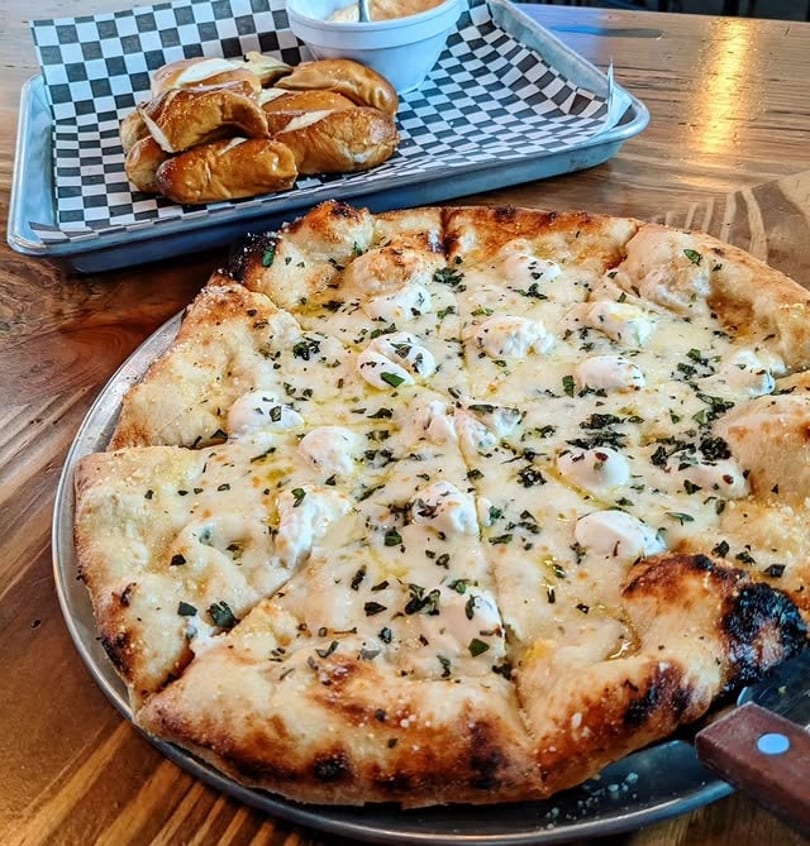 White pizza with dollops of ricotta and herbs, alongside a tray of pretzel bites and dip.