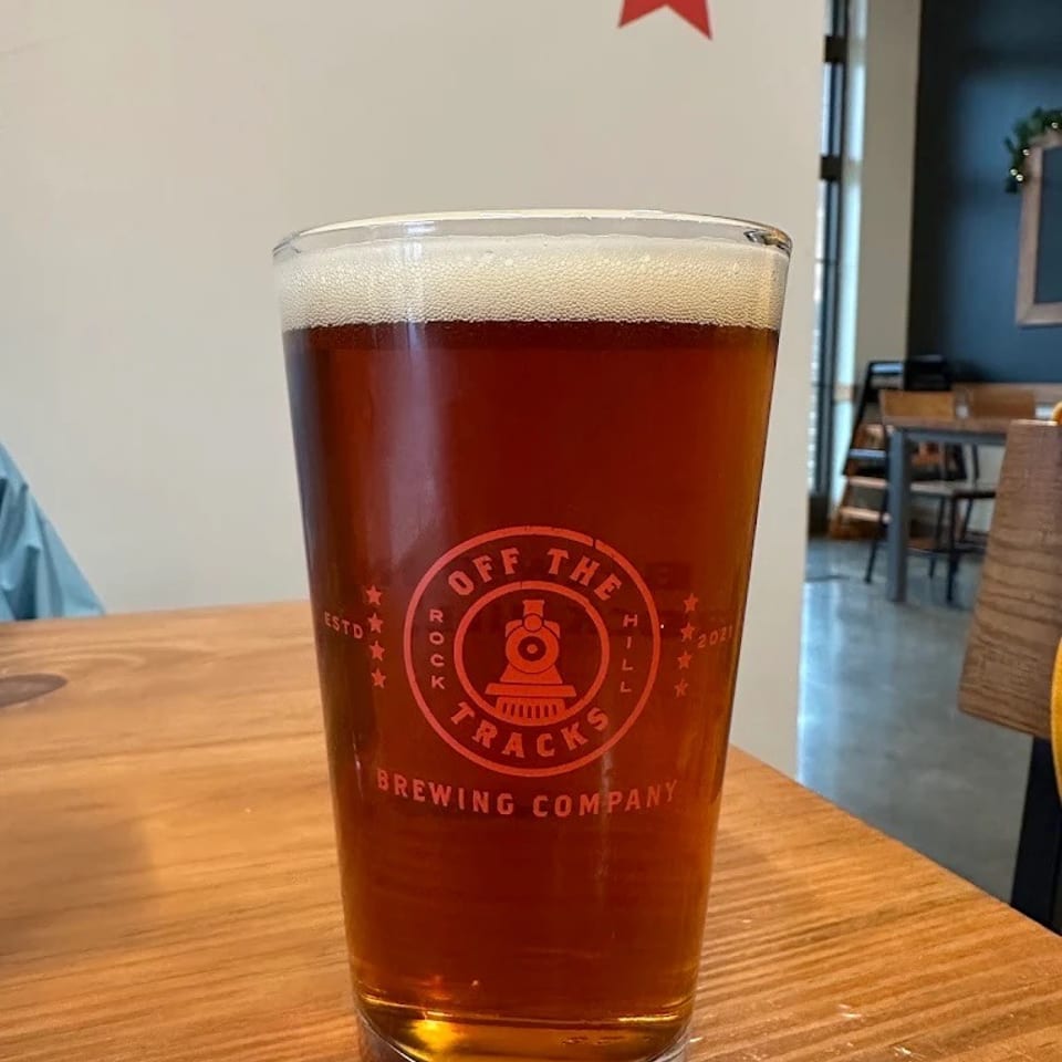 A pint glass of amber beer from Off The Tracks Brewing Company on a wooden table.