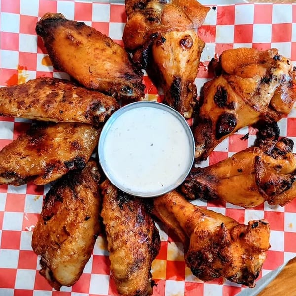 Grilled chicken wings arranged around a small cup of ranch dressing on red and white checkered paper.