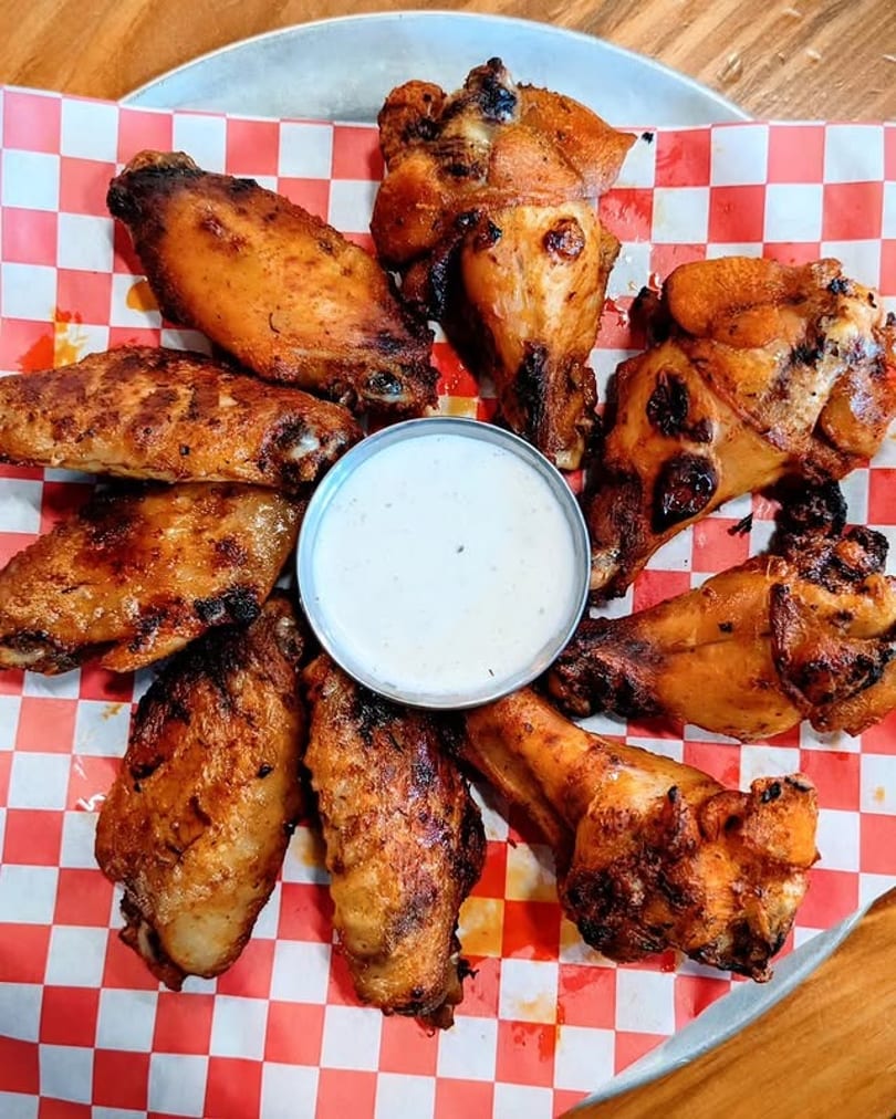 Grilled chicken wings arranged around a small cup of ranch dressing on red and white checkered paper.