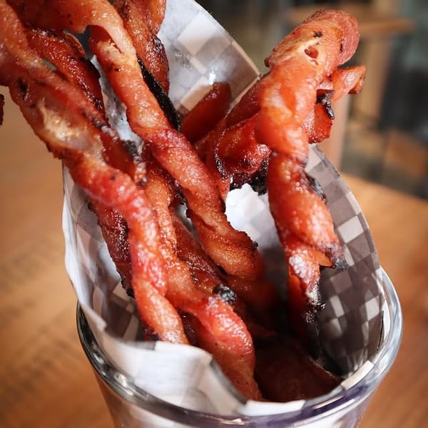 Crispy twisted bacon strips served upright in a glass with checkered paper.