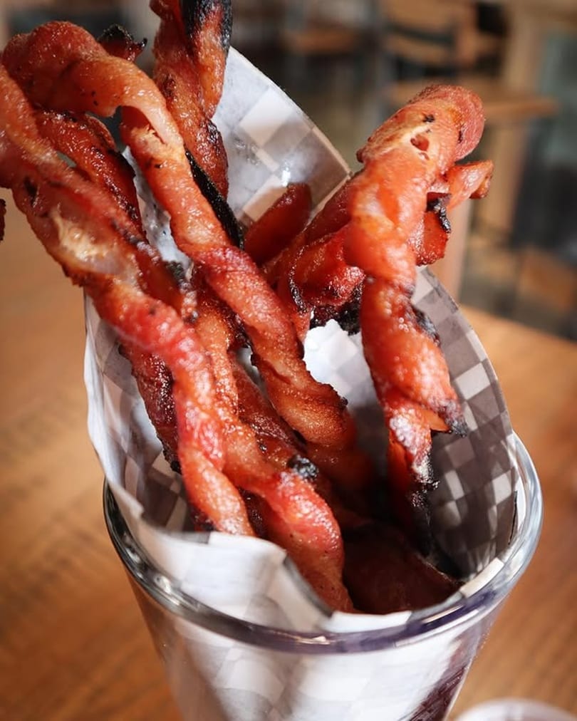 Crispy twisted bacon strips served upright in a glass with checkered paper.