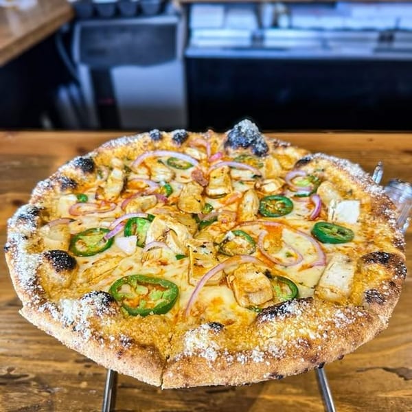 A chicken, red onion, and jalapeño pizza with a parmesan crust on a metal stand.