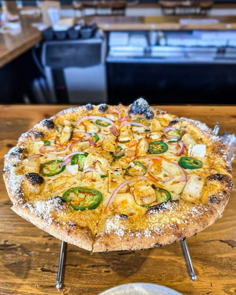 A chicken, red onion, and jalapeño pizza with a parmesan crust on a metal stand.