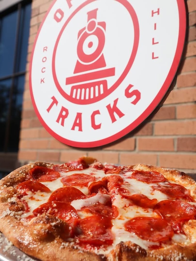 Pepperoni pizza with a golden crust and melted cheese, in front of the Rock Hill Tracks logo.
