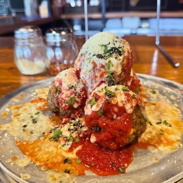 Four large meatballs covered in marinara sauce, melted cheese, and fresh parsley on a metal plate.