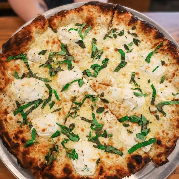 White pizza with ricotta cheese, mozzarella, and fresh basil on a metal tray.