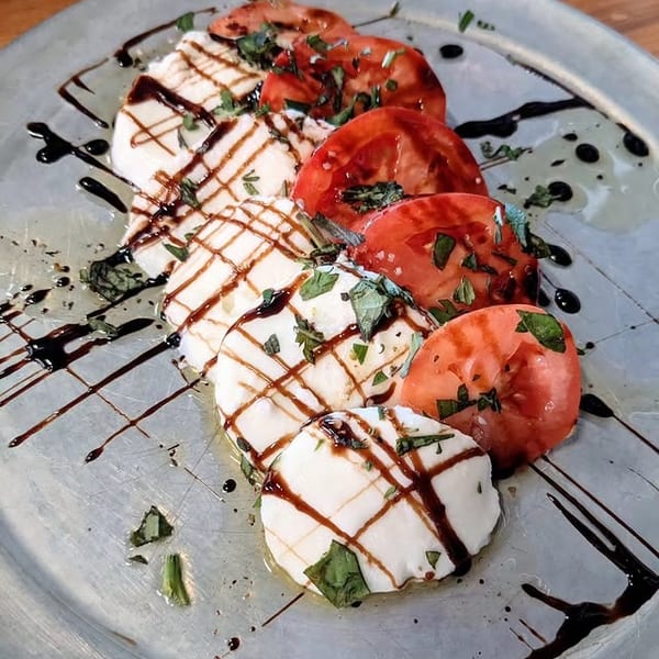 Caprese salad with sliced mozzarella, tomatoes, basil, and balsamic glaze on a silver plate.