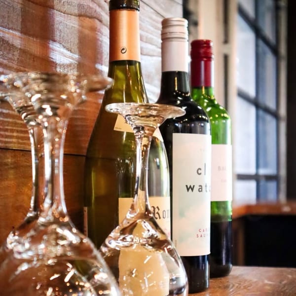 Wine bottles and inverted wine glasses are displayed on a wooden surface against a wood-paneled wall.